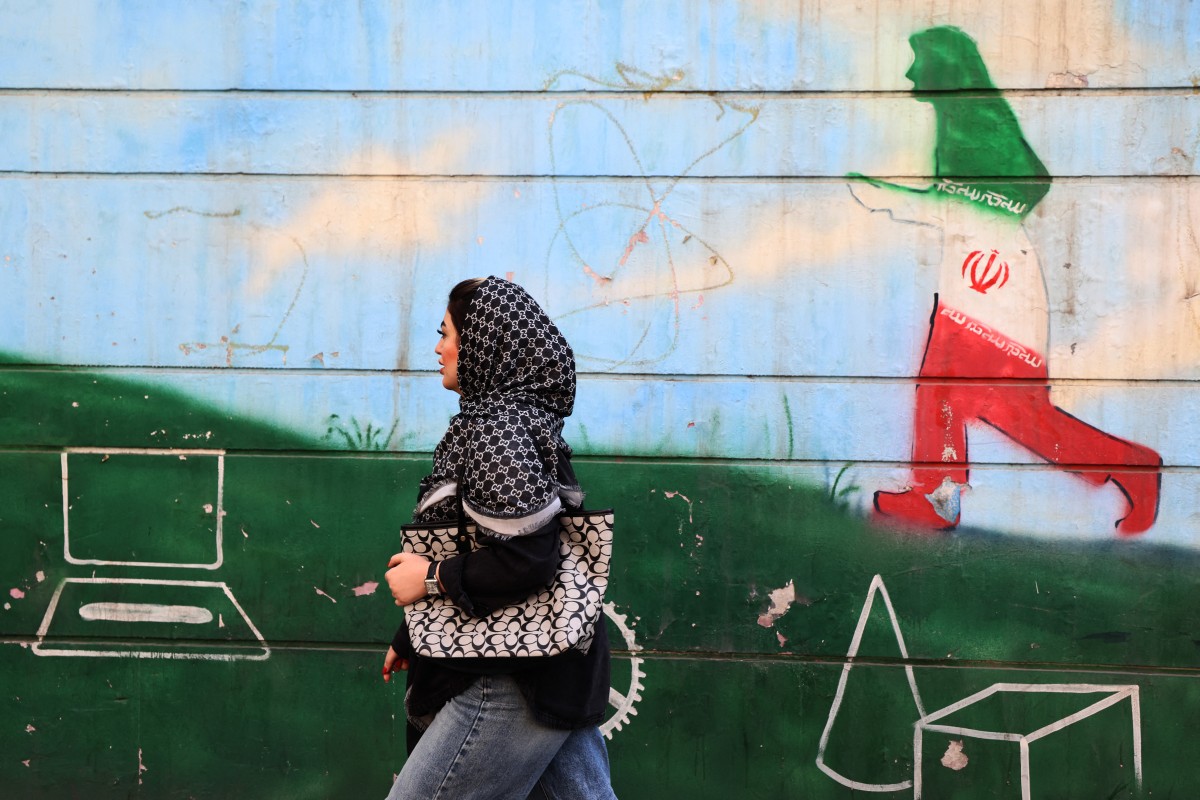 سيدة تمر أمام جدارية بألوان العلم الإيراني في طهران. (أ ف ب)