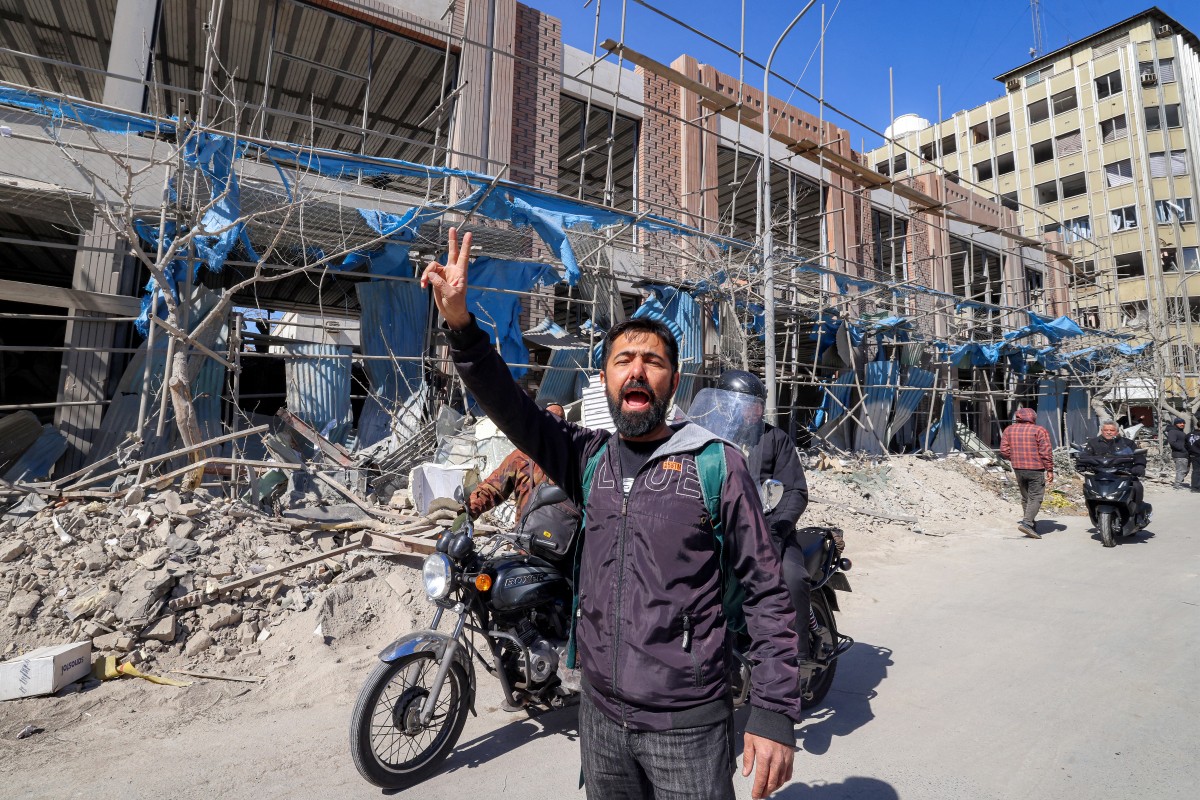 رجل إيراني يرفع شارة النصر بجوار مبانٍ منهارة ومتضررة بالقرب من ميدان فردوسي في طهران. (أ ف ب)