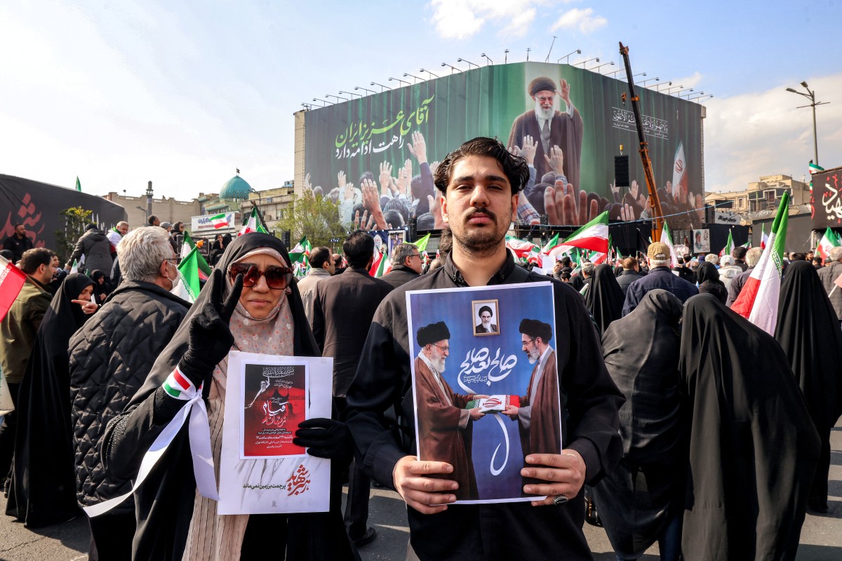 رجل يقف مع صورة للمرشد الأعلى الإيراني الجديد آية الله مجتبى خامنئي (يمين)، بجانب والده الراحل علي خامنئي، خلال تجمع لدعمه في وسط طهران (أ ف ب)