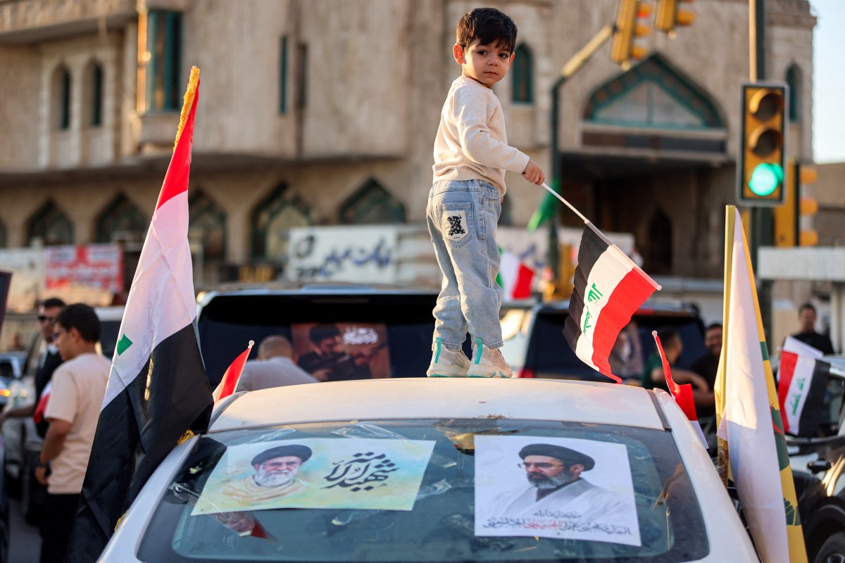 طفل يلوّح بالعلم العراقي من فوق سيارة تحمل صور المرشد الأعلى الإيراني الراحل علي خامنئي ونجله مجتبى خامنئي، في ساحة التحرير وسط بغداد. (أ ف ب)