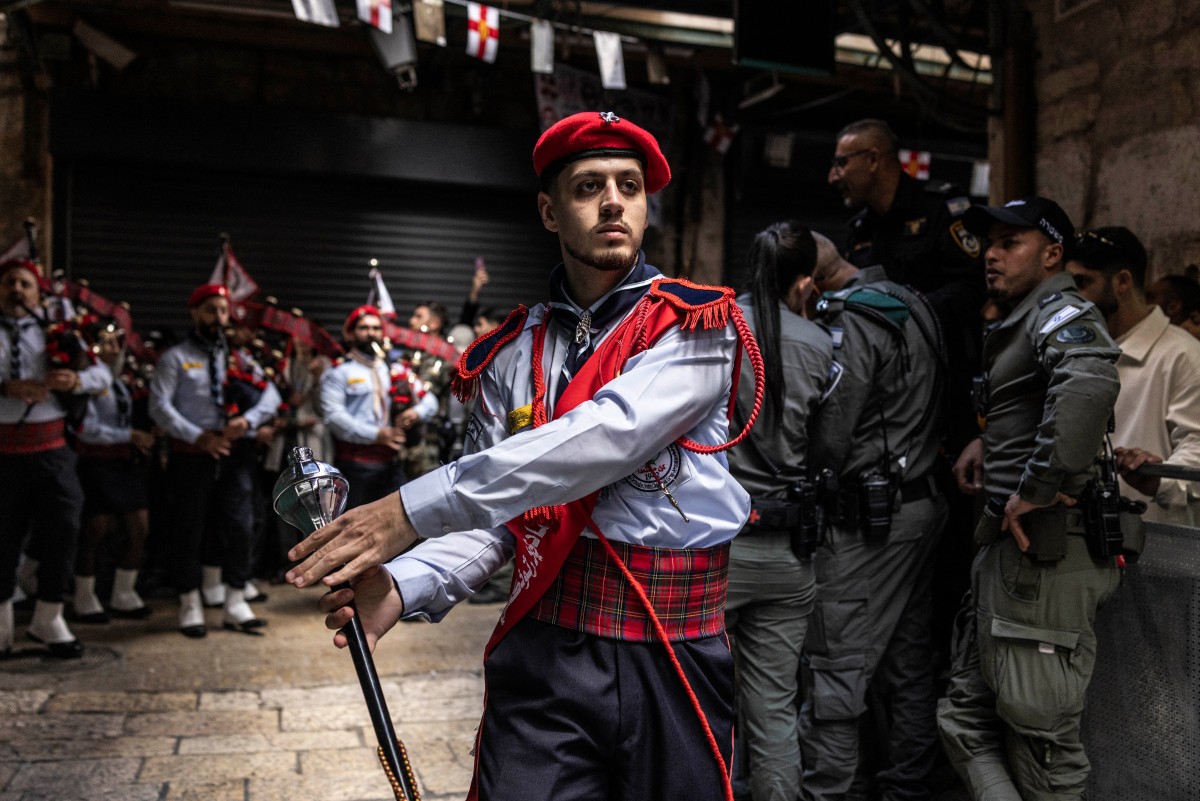 عناصر من الشرطة الإسرائيلية بجانب أحد أفراد فرقة الكشافة الموسيقية المشاركة في مسير الشعلة المقدسة، في القدس. (أ ف ب)