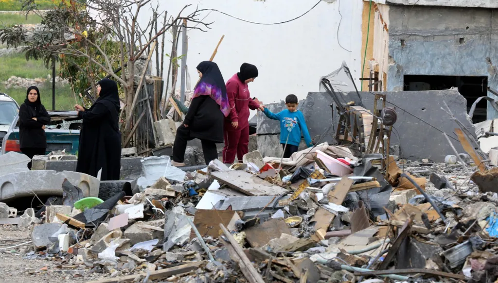 أشخاص يقفون على أنقاض منزل مدمر بعد عودتهم إلى مدينة النبطية في جنوب لبنان (أ ف ب). 