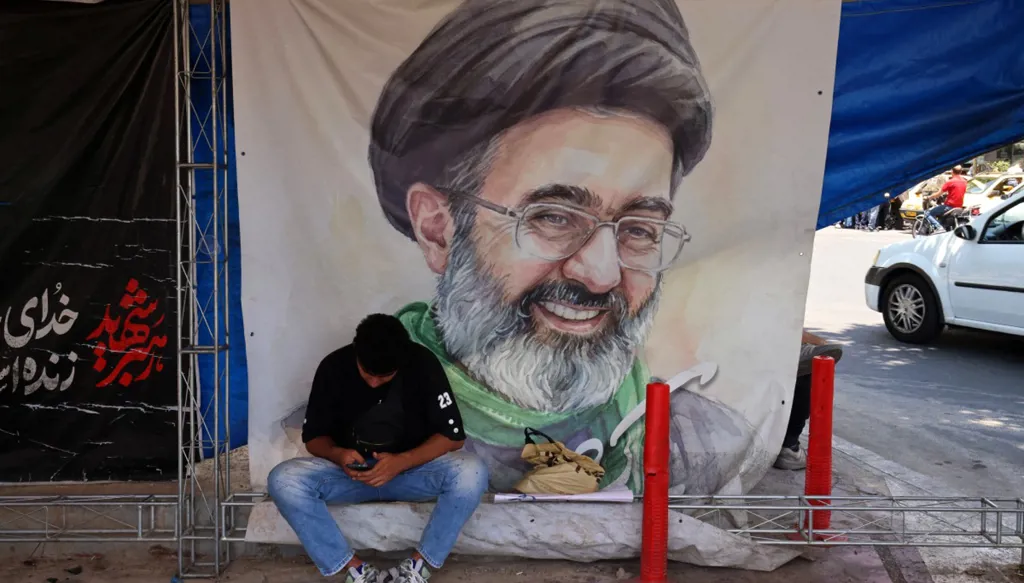 شخص يجلس في طهران وخلفه صورة للمرشد الإيراني (أ ف ب)