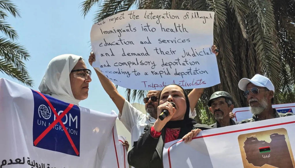 ليبيون ومتضامنون يتظاهرون أمام مقر المنظمة الدولية للهجرة في طرابلس، مطالبين بإعادة توطين المهاجرين غير النظاميين واللاجئين.