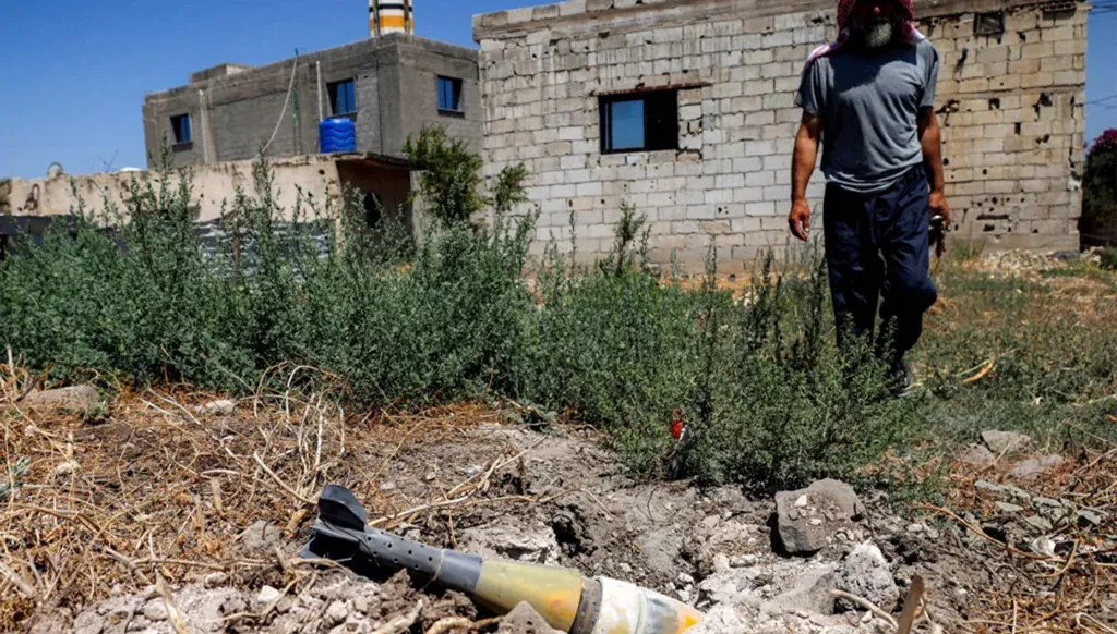 A man stands near an unexploded artillery shell that landed during an overnight Israeli bombardment targeting the village of Abidin in Syria's southwestern Daraa province, near the Golan Heights, on June 29, 2026. (AFP)