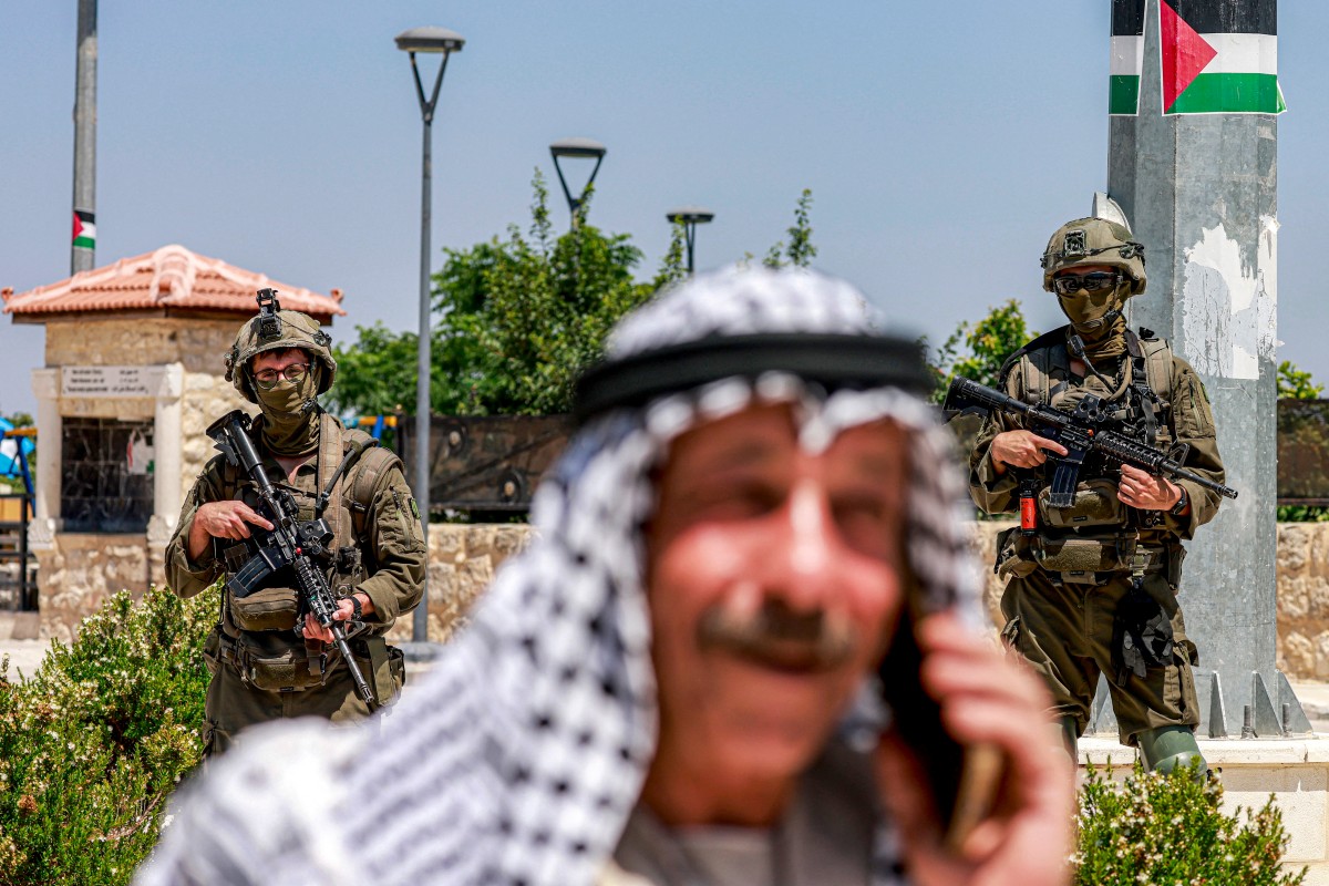 فلسطيني يتحدث على الهاتف وخلفه جنديان إسرائيليان في الضفة (أ ف ب)