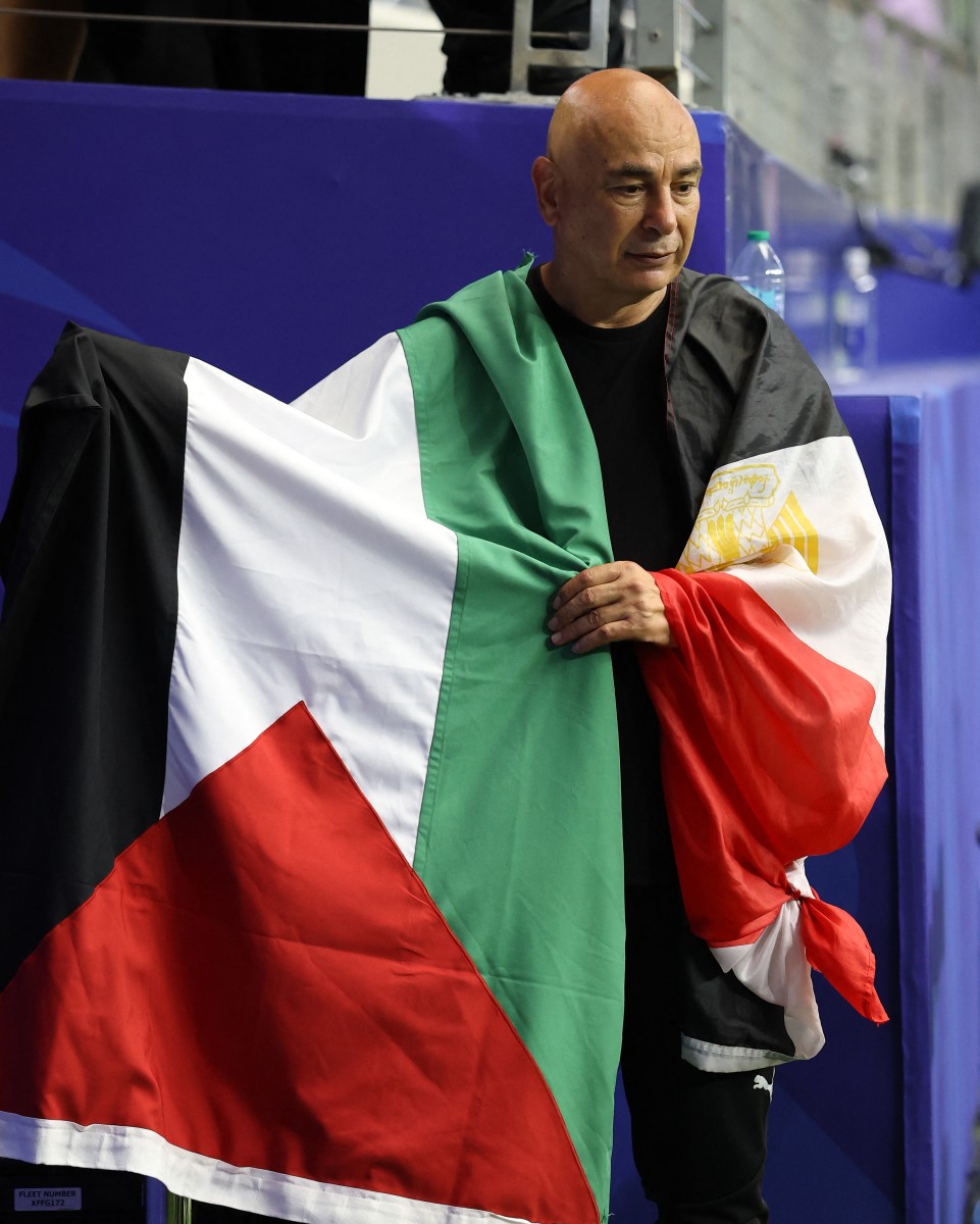 مدرب منتخب مصر حسام حسن رافعاً العلمين المصري والفلسطيني. (أ ف ب)