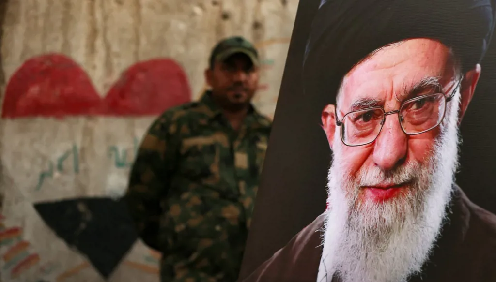 عنصر في الحشد الشعبي يقف خلف صورة المرشد الإيراني الراحل علي خامنئي في كربلاء عشية مراسم تشييعه، في 7 تموز/يوليو 2026. (أ ف ب)