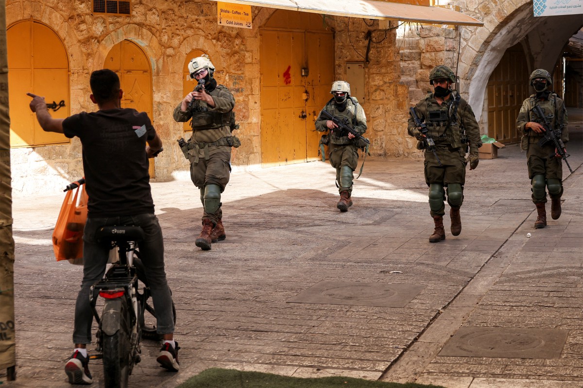 جنود إسرائيليون يجبرون فلسطينياً على مغادرة سوق البلدة القديمة في الخليل. (أ ف ب)