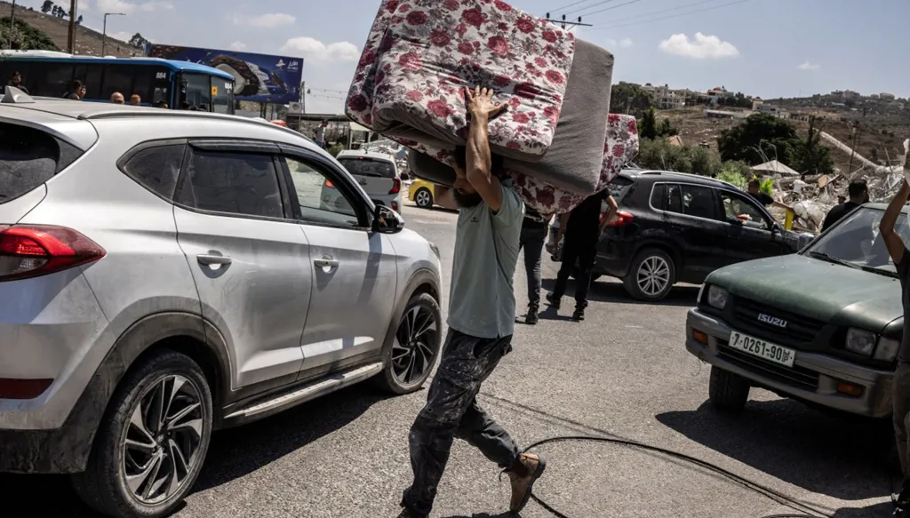 مواطن فلسطيني يحمل فراشاً في جنين (أ ف ب).