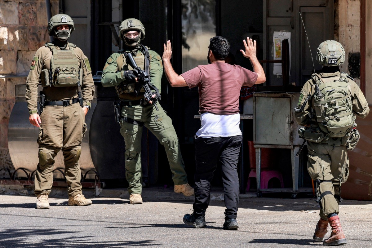 فلسطيني يرفع ذراعيه في مواجهة جنود الجيش الإسرائيلي خلال عملية عسكرية في نابلس، بالضفة الغربية المحتلة، 2 آب/أغسطس 2026. (أ ف ب)