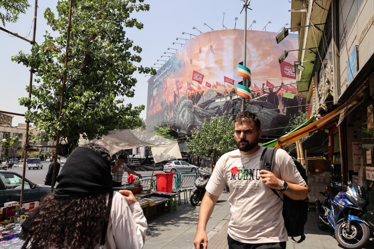 إيرانيون يمرّون أمام لوحة مناهضة للولايات المتحدة في ساحة انقلاب وسط طهران، في 3 آب/أغسطس 2026. (أ ف ب)