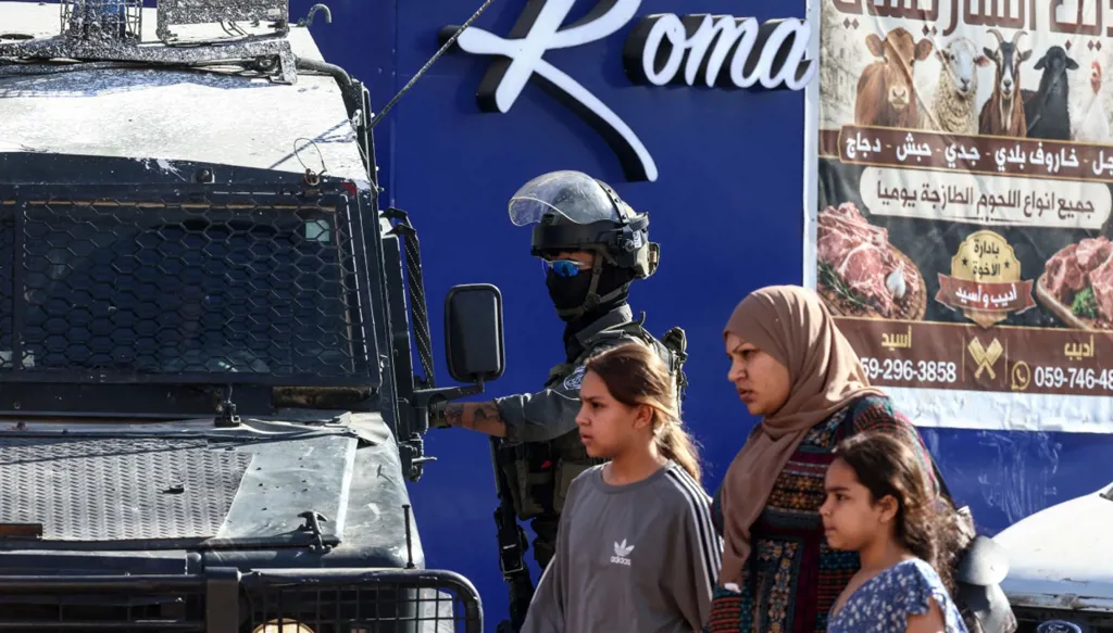 سيدة وطفلان يمرّون قرب جندي إسرائيلي خلال اقتحام مخيم قلنديا شمال القدس، 5 آب/أغسطس 2026. (أ ف ب)