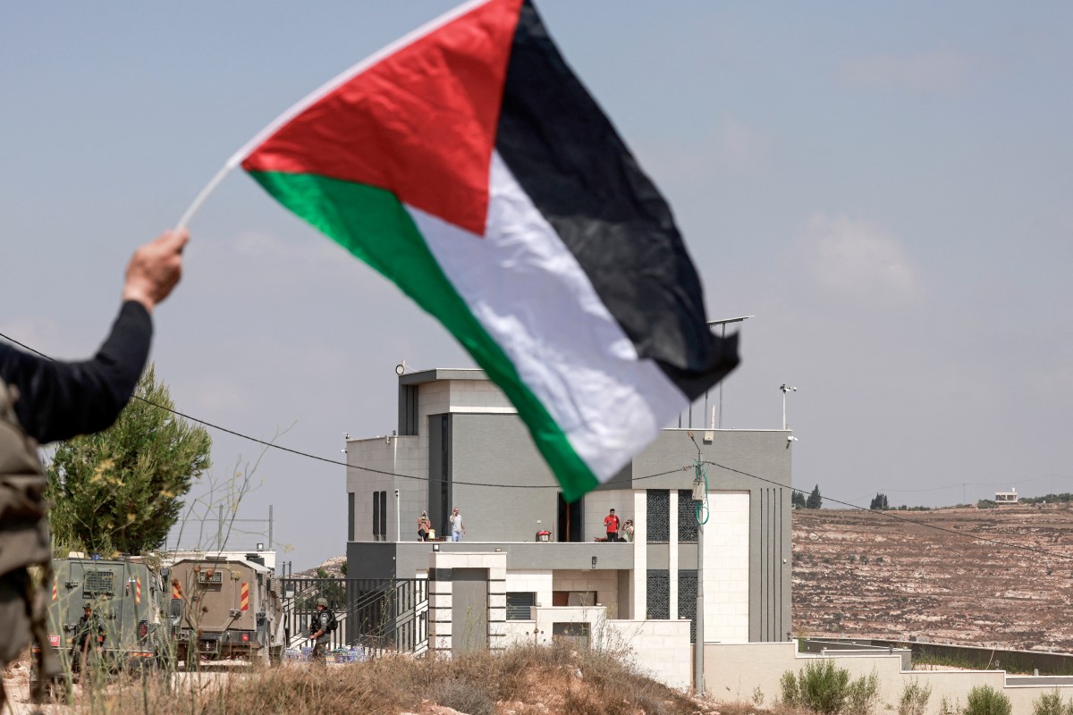 رجل يلوّح بالعلم الفلسطيني أمام منزل يحاصره مستوطنون إسرائيليون في قرية قُصرة جنوب نابلس، 14 آب/أغسطس 2026. (أ ف ب)  