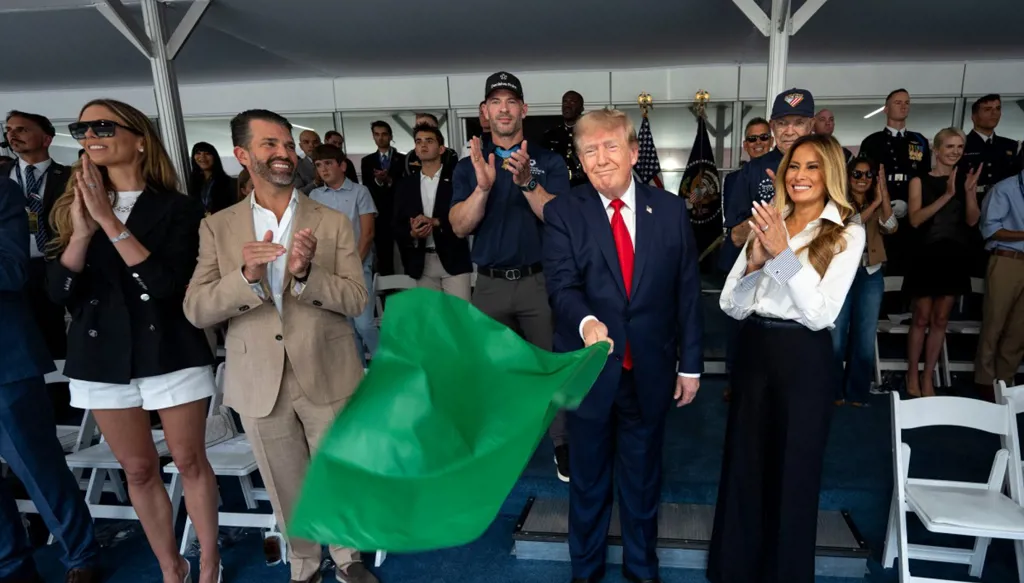 الرئيس الأميركي دونالد ترامب يلوّح بالعلم الأخضر إيذاناً بانطلاق سباق للسيارات في شوارع واشنطن، وإلى جانبه السيدة الأولى ميلانيا ترامب، 23 آب/أغسطس 2026. (أ ف ب)