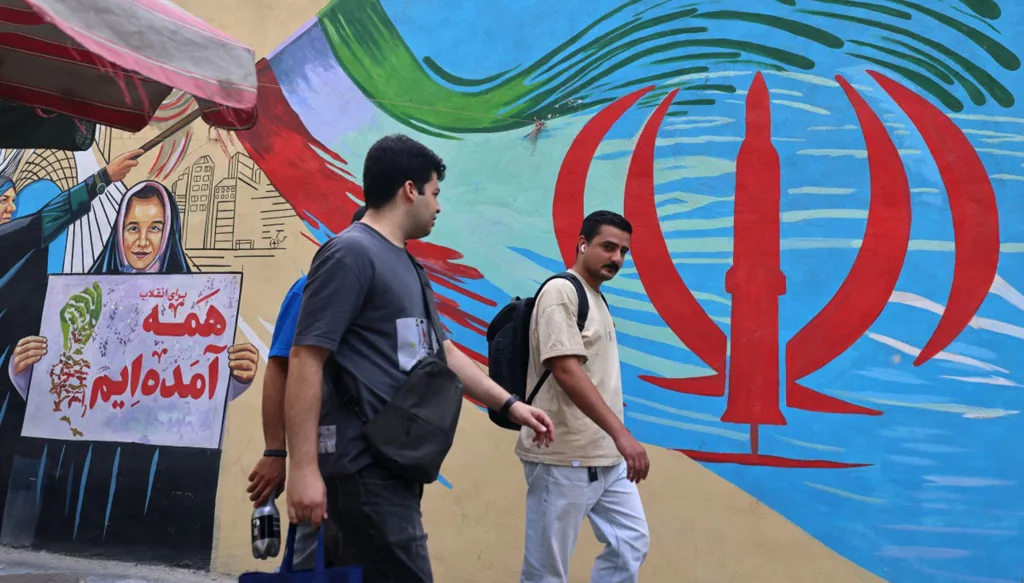شابان يمران أمام جدارية تُظهر صاروخاً يتوسط شعار الجمهورية الإسلامية الإيرانية، في وسط طهران في 31 آب/أغسطس 2026. (أ ف ب)