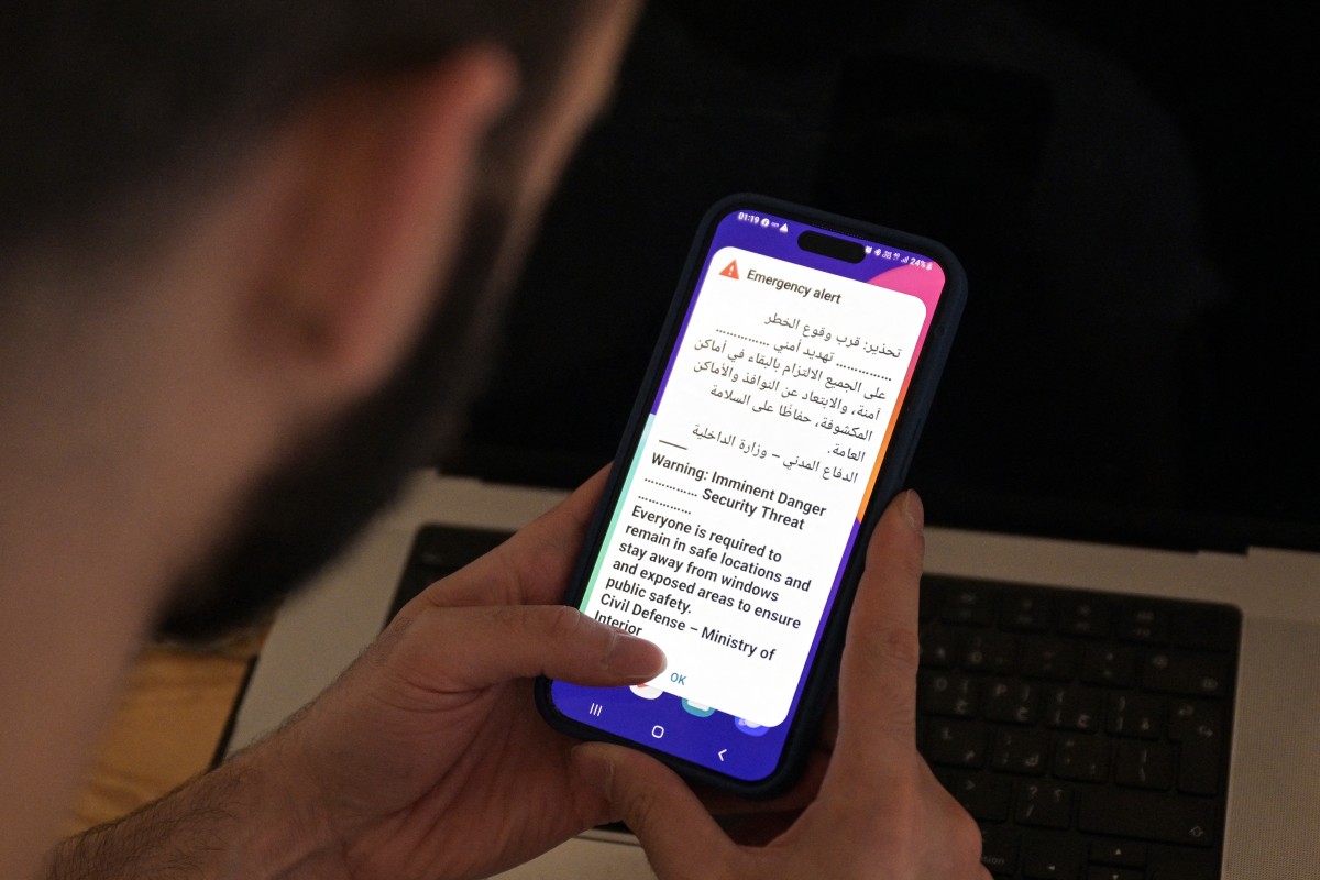 رجل كويتي يحمل هاتفه المحمول الذي يعرض رسالة تنبيه، بينما تدوي صفارات الإنذار خلال هجوم إيراني بصواريخ أو طائرات مسيّرة، في مدينة الكويت. (أ ف ب)