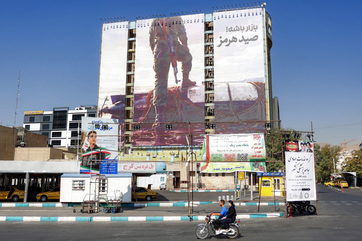 دراج على دراجة نارية قرب لوحة عملاقة على واجهة مبنى، تُظهر عنصراً في الحرس الثوري الإيراني يضع قدمه على مسيّرة بحرية أميركية يُقال إن إيران استولت عليها في مضيق هرمز، طهران، 24 أيلول/سبتمبر 2026. (أ ف ب)
