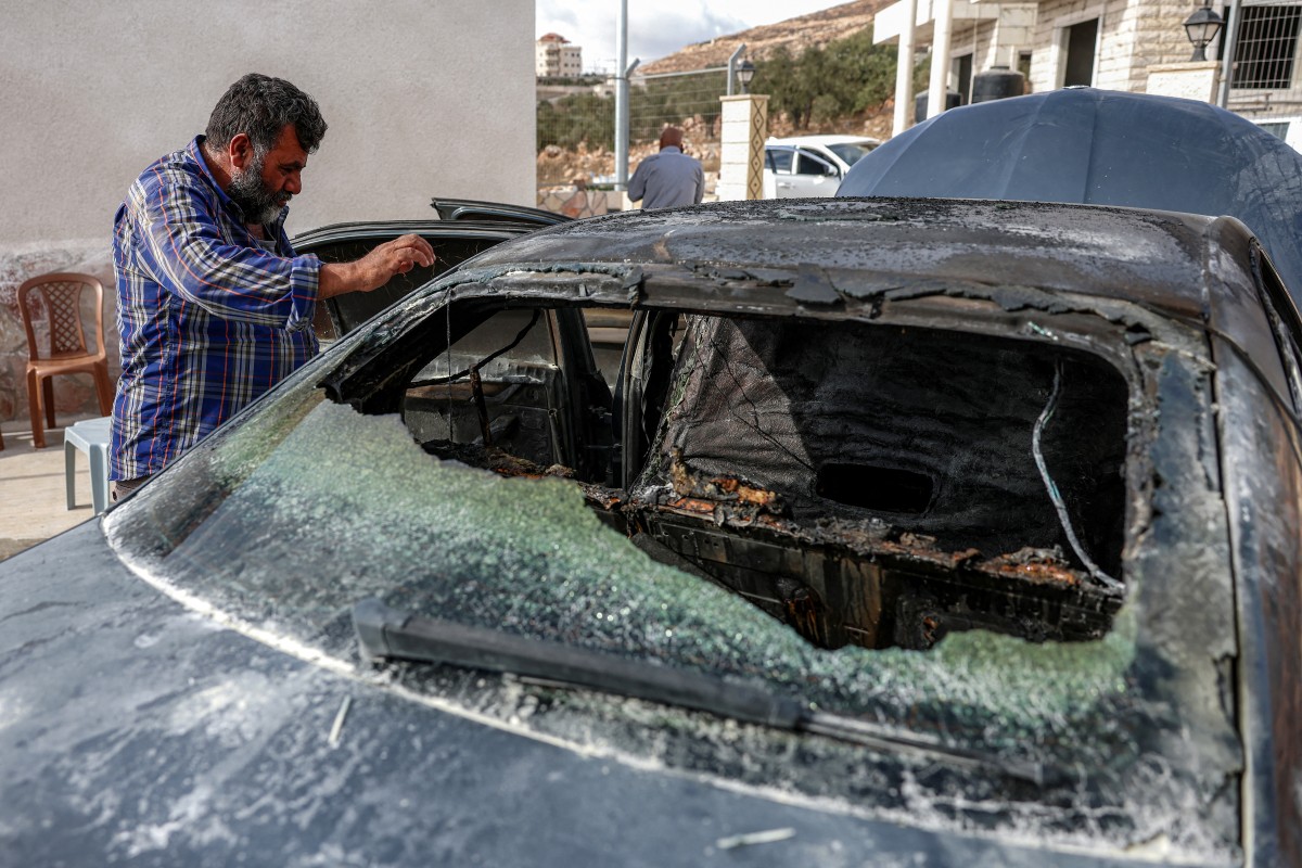 فلسطيني إلى جانب مركبته بعدما أحرقها مستوطنون (أ ف ب)