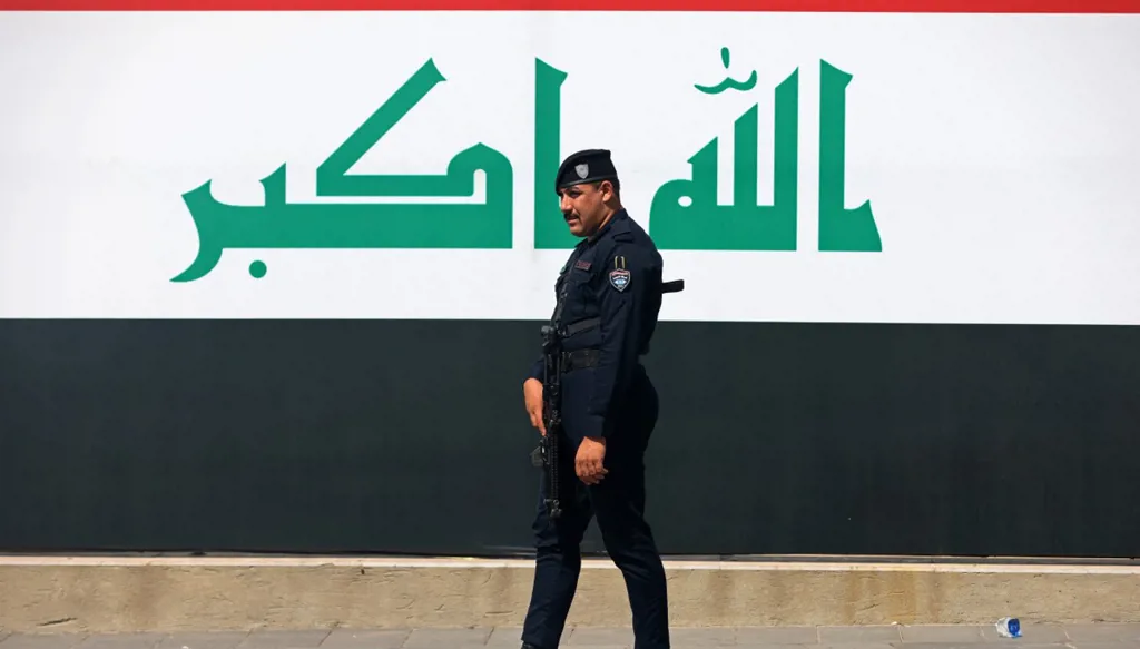 شرطي يمر أمام علم عراقي عملاق في ميدان التحرير في بغداد (أ ف ب).