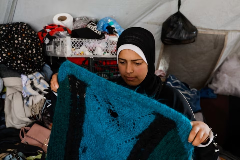 أماني أبو سلمي تحمل ملابس صوفية ممزقة داخل خيمة في خان يونس جنوب قطاع غزة، في 26 نيسان/أبريل 2026 (رويترز)