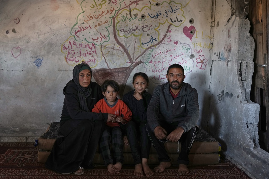 Amani and Mohammed Halawa pose for a picture with their children, Aya, 13, and Bashir, 10, inside their partially collapsed home, with a tree and messages of longing and hope painted on the wall behind them, Jabaliya, Gaza City, Tuesday, Nov. 25, 2025.(AP Photo/Jehad Alshrafi)