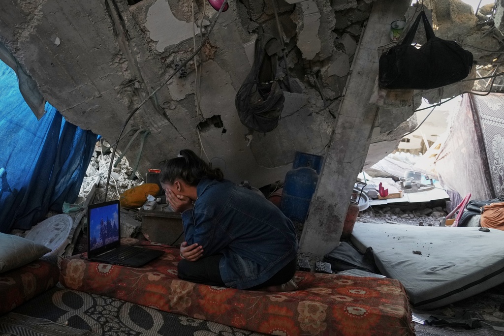 Bisan Taroush watches a movie on a laptop beneath the partially collapsed roof of her home, carrying on with daily life amid the ruins, in Jabaliya, Gaza City, Tuesday, Nov. 11, 2025. (AP Photo/Jehad Alshrafi)