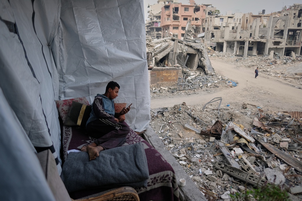 Omar Qutay sits on a bed placed on the balcony of his partially destroyed home in the Al-Karama neighborhood of Gaza City, Wednesday, Nov. 24, 2025. (AP Photo/Jehad Alshrafi)