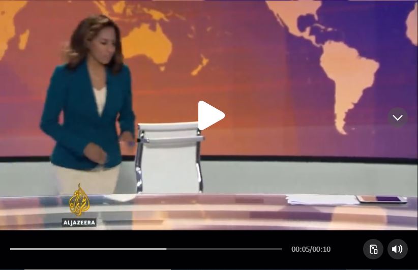 لقطة من الفيديو تظهر المذيعة وهي تعود الى الطاولة للجلوس على الجهة الخلفية للكرسي الابيض