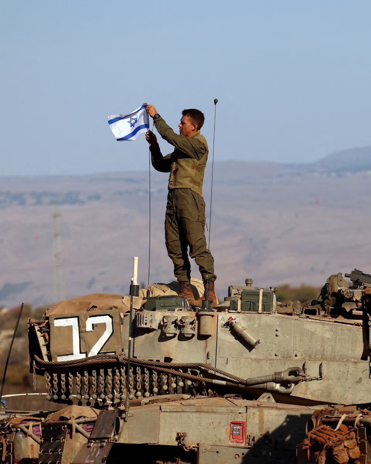 جندي يرفع العلم الإسرائيلي على دبابة خلال تدريب عسكري قرب الحدود الإسرائيلية مع لبنان (رويترز)