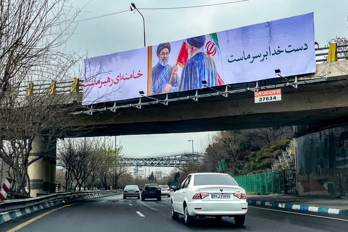 لوحة إعلانية تصور المرشد الأعلى الإيراني الراحل علي خامنئي وهو يسلم ابنه والمرشد الأعلى الجديد مجتبى خامنئي علمًا إيرانيًا في طهران في 10 مارس 2026 (أ ف ب)