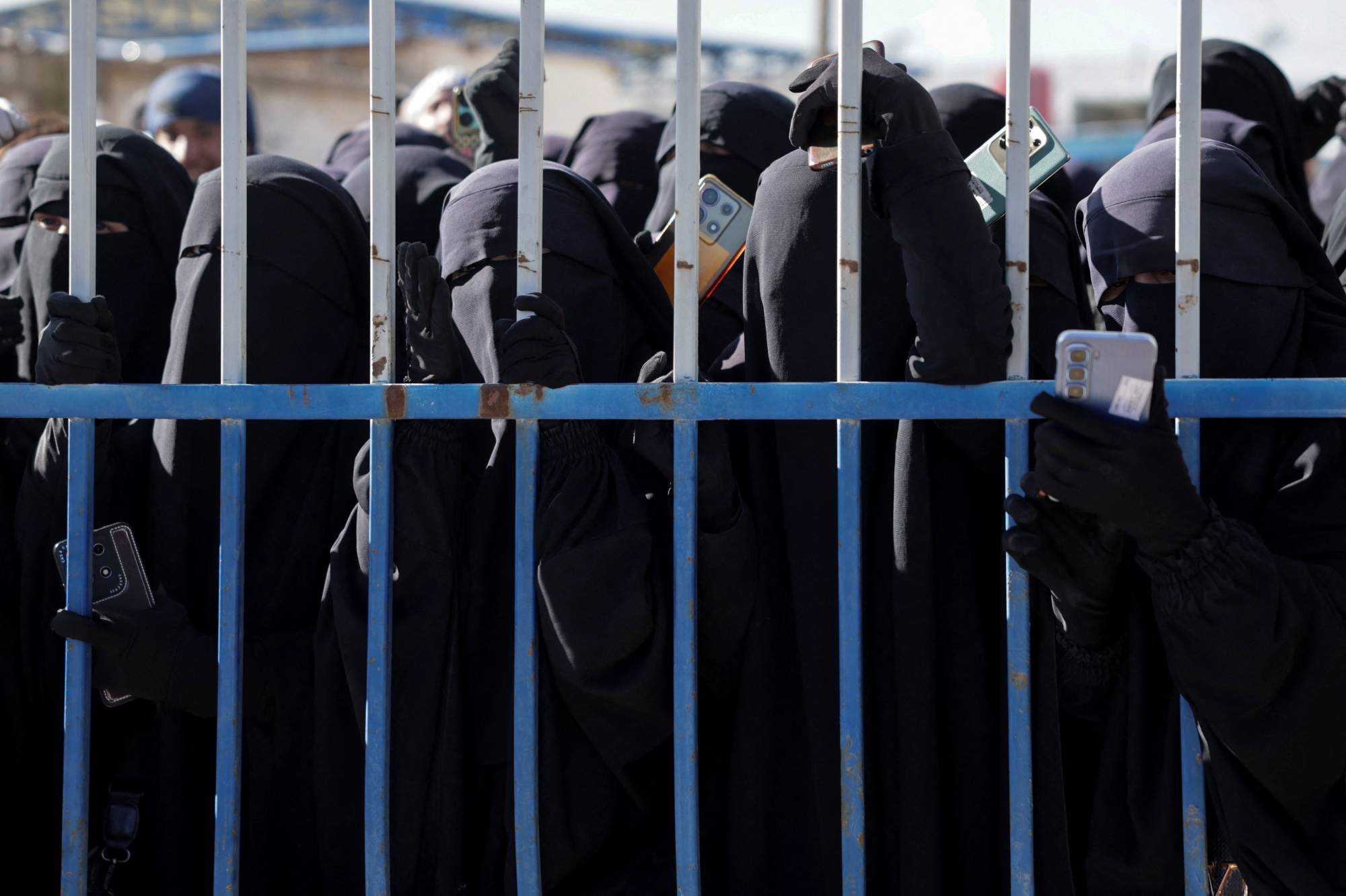 مجموعة من السجينات ينظرن عبر سياج في مخيم الهول، بعد سيطرة الحكومة السورية عليه إثر انسحاب قوات سوريا الديموقراطية، الحسكة، سوريا، 21 كانون الثاني/يناير 2026. (رويترز)  