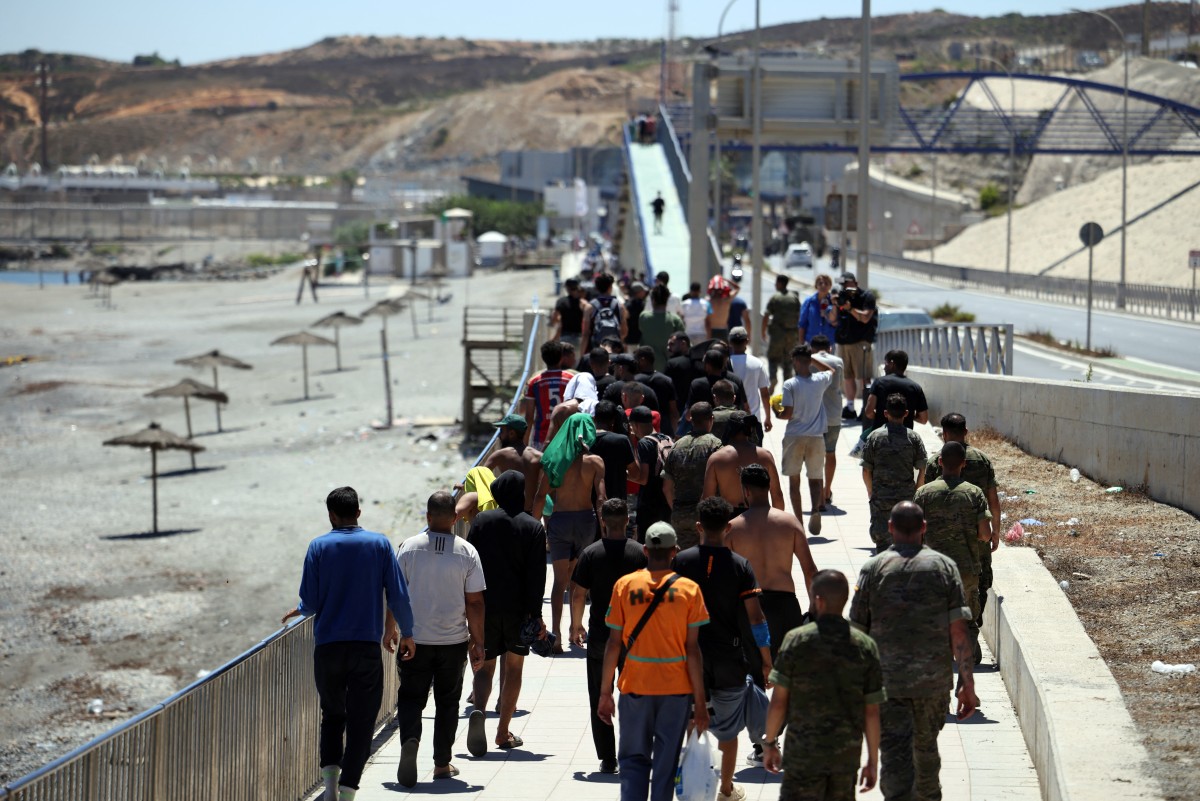 مجموعة من المهاجرين تقترب من نقطة الحدود للعودة إلى المغرب، برفقة جنود مشاة إسبان، في منطقة في 2 أغسطس 2026 (أ ف ب)