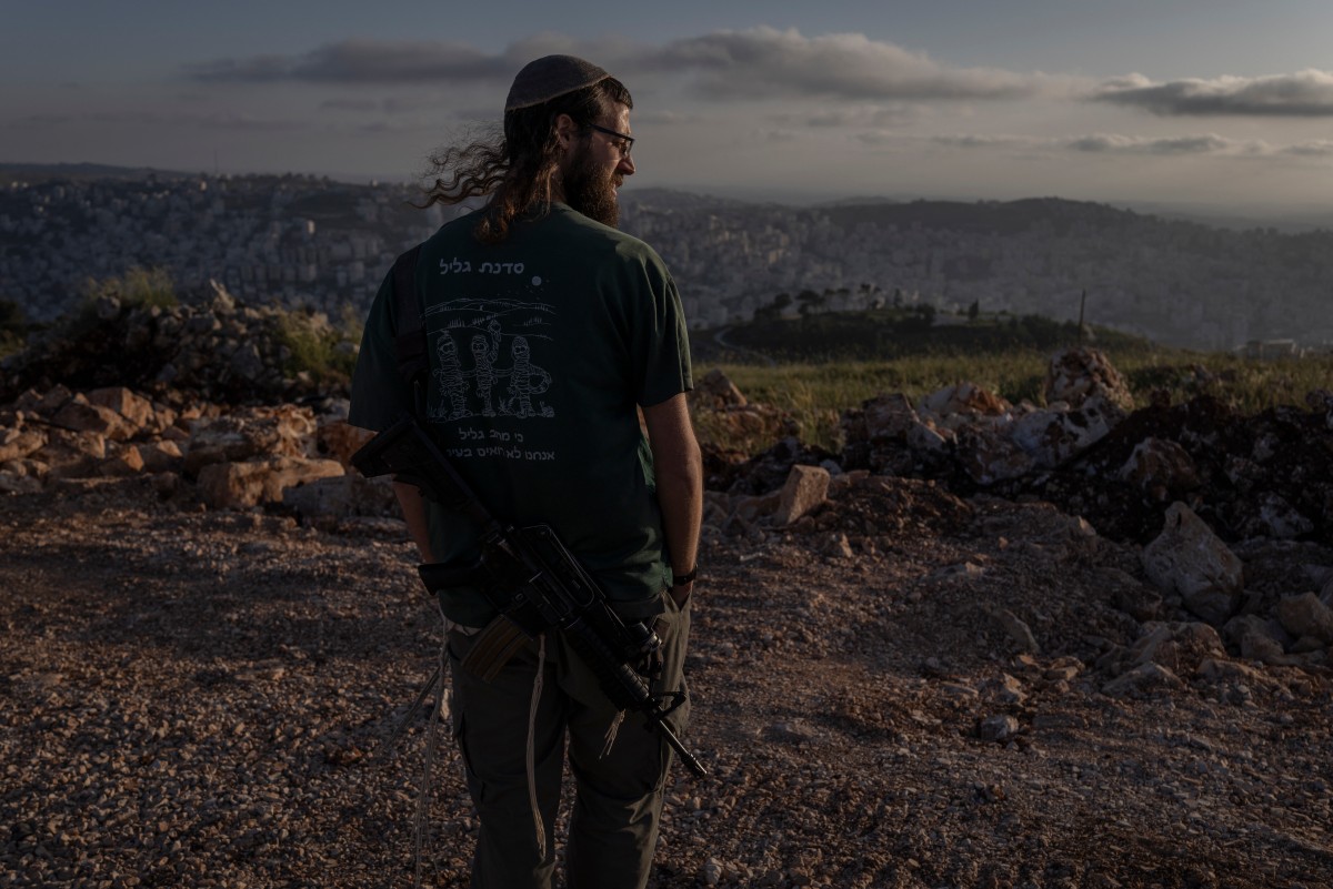 مستوطن إسرائيلي مسلح يقف مطلاً على نابلس من مستوطنة هار إيبال (جبل إيبال) في الضفة الغربية المحتلة، في 28 نيسان/أبريل 2026 (أ ف ب)