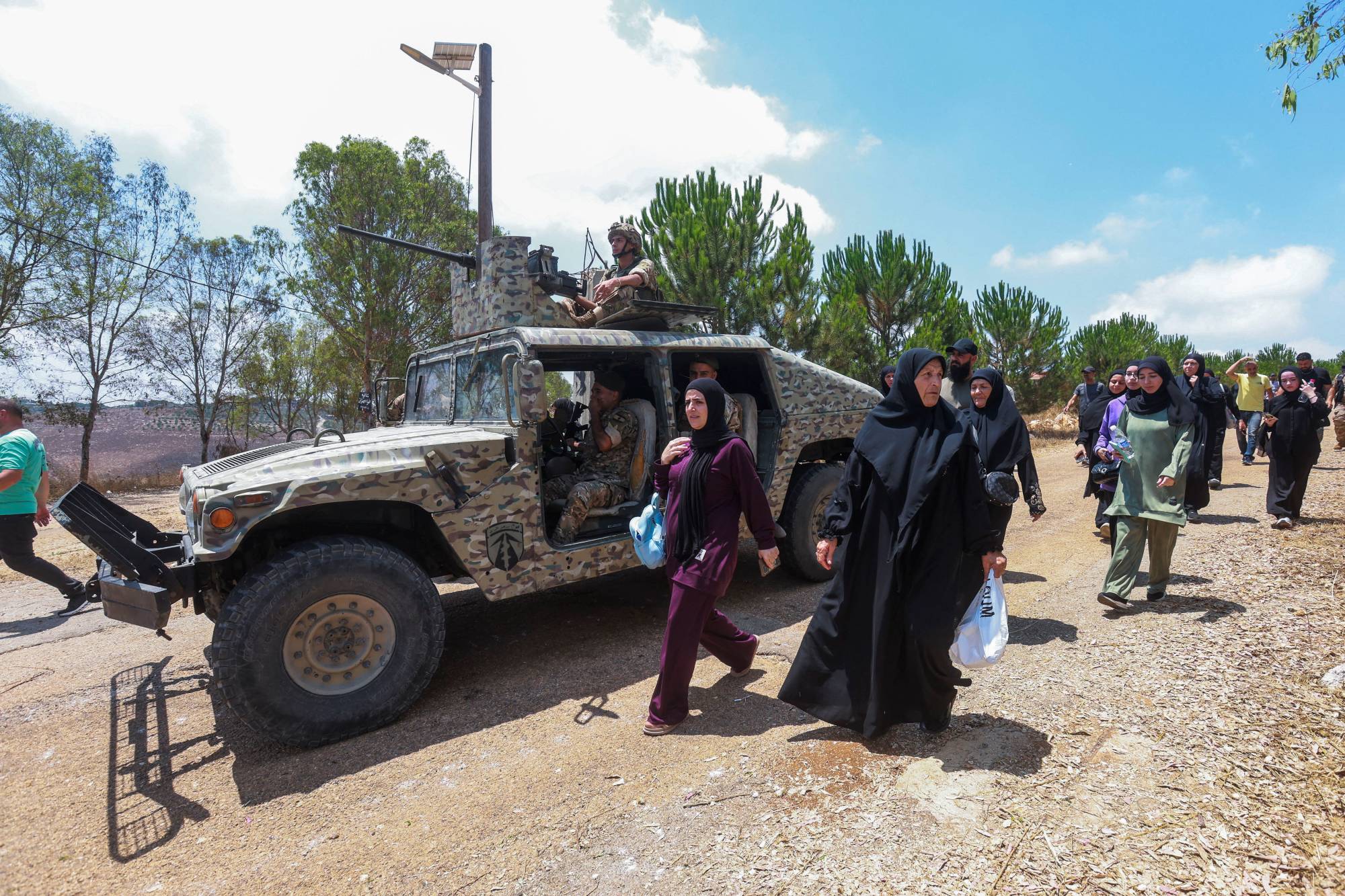 مواطنون لبنانيون يسيرون إلى جانب آلية للجيش اللبناني محاولين دخول بلدة زوطر الغربية (رويترز)