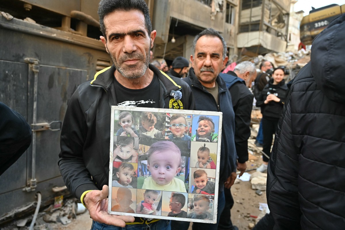 رجل يحمل صوراً لأطفال قُتلوا خلال غارات إسرائيلية على محلة حي السلم في الضاحية الجنوبية لبيروت (أ ف ب)