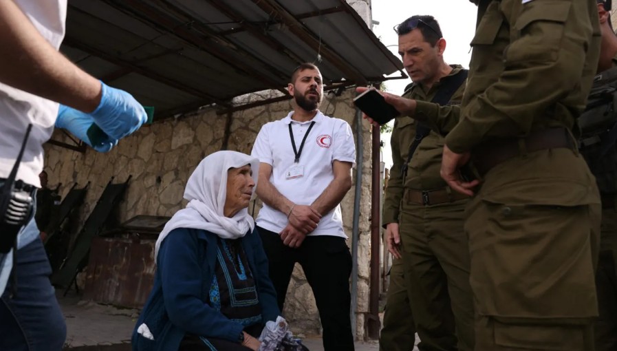 الضابط الإسرائيلي هشام إبراهيم، رئيس وحدة تنسيق أنشطة الحكومة الإسرائيلية في الأراضي الفلسطينية، يتحدث إلى امرأة فلسطينية مسنة على كرسي متحرك عند نقطة تفتيش عسكرية في بيت لحم، بالضفة الغربية المحتلة، في 28 مارس/آذار 2025