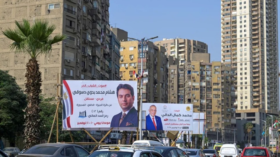 سائقون يمرون أمام لوحة إعلانية لحملة انتخابية لمرشحي الانتخابات البرلمانية المصرية في مدينة الجيزة التوأم بالعاصمة القاهرة (أ ف ب)