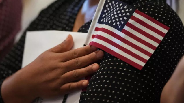 امرأة تمسك بعلم الولايات المتحدة بينما تستعد هي والمتقدمون من بلدان أخرى لأداء قسم الجنسية (أ ب)