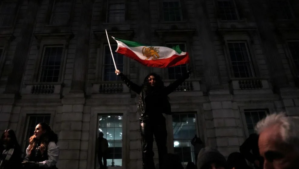 رفع أحد المتظاهرين علم إيران الذي يعود لما قبل ثورة 1979، والذي يحمل شعاري الأسد والشمس، خلال مسيرة تضامنية مع الانتفاضة الإيرانية، نظمها المجلس الوطني للمقاومة الإيرانية، في وايتهول بوسط لندن. (أ ف ب)