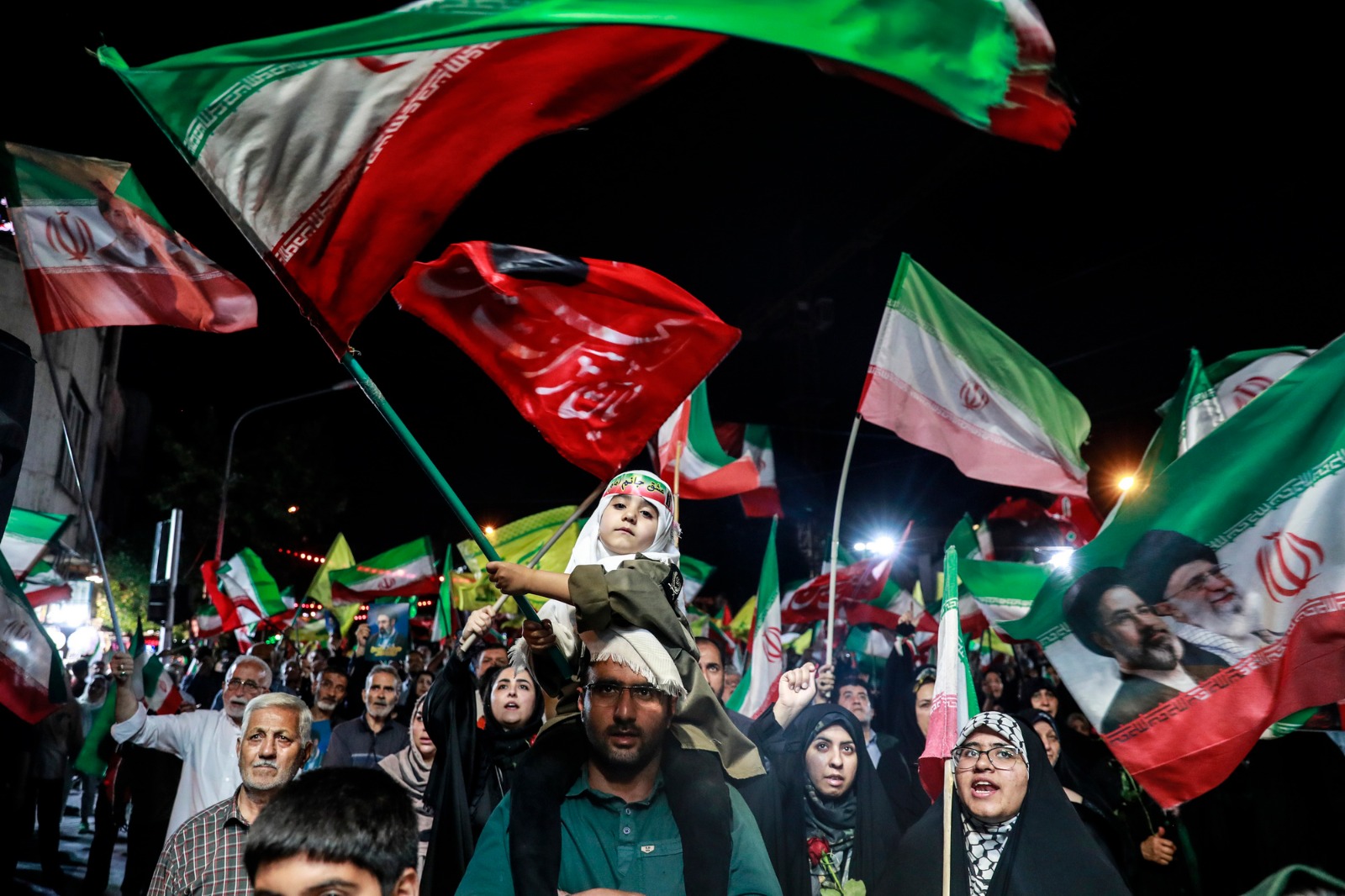 طفل يجلس على كتفي رجل ويلوح بعلم إيران بين مؤيدين للحكومة خلال تجمع نظمته السلطات في طهران. (رويترز)