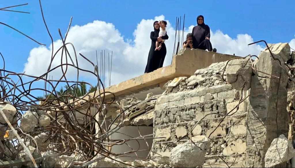 أفراد عائلة يقفون على سطح منزلهم المدمّر (أحمد منتش). 