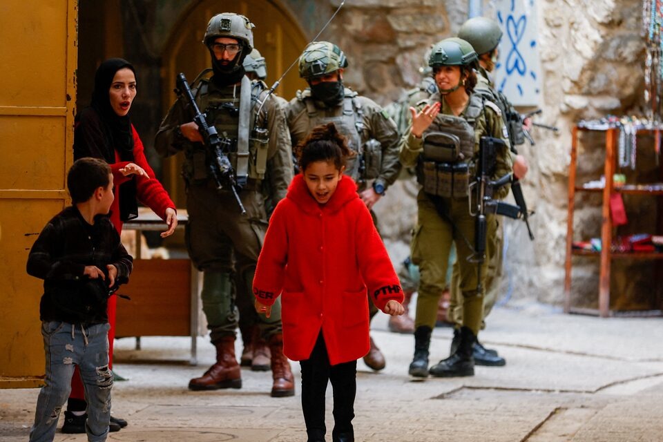امرأة فلسطينية تبعد أطفالها عن مجموعة من الجنود الإسرائيليين خلال جولة أسبوعية للمستوطنين في مدينة الخليل بالضفة الغربية. (رويترز)