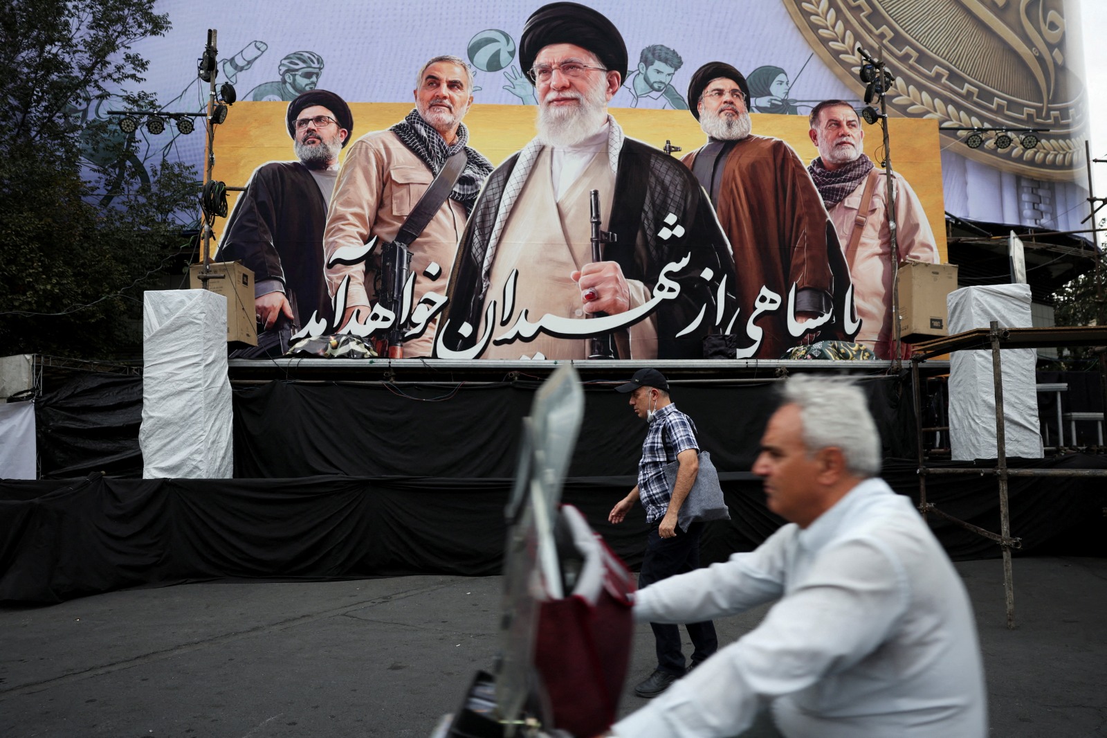 رجل يمر أمام لوحة تحمل صور علي خامنئي وحسن نصرالله وقاسم سليماني في طهران في 6 تشرين الأول/أكتوبر 2026. (وانا عبر رويترز)