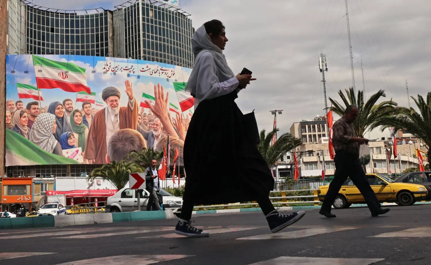 إيرانيون يمرون بلوحة إعلانات ضخمة لعلي خامنئي في ساحة ولي العصر بطهران، 19 أبريل 2026. (فرانس برس)