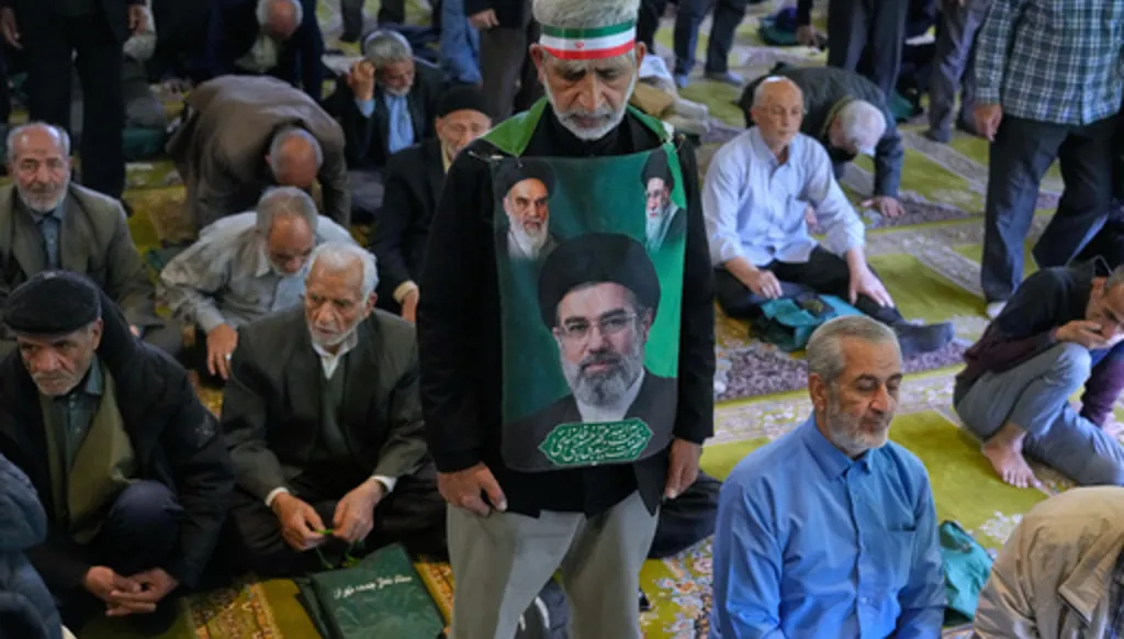 An Iranian worshipper wears a banner showing portraits of the Supreme Leader Ayatollah Mojtaba Khamenei, bottom, late Supreme Leader Ayatollah Ali Khamenei, top right, and the late revolutionary founder Ayatollah Khomeini, during Friday prayers ceremony at the Tehran University campus, in Tehran, Iran, Friday, April 24, 2026. (AP Photo/Vahid Salemi)