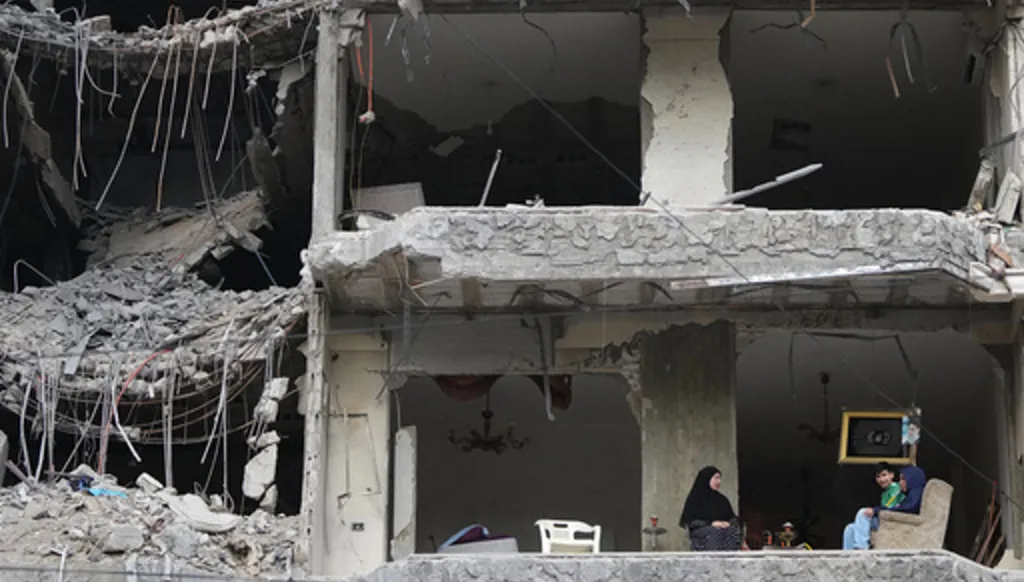 The wife and children of Fadi Al Zein, who lost both his homes in Israeli strikes in his village of Khiam and in Dahiyeh, sit on the balcony of their heavily damaged apartment building in Beirut's southern suburbs, Lebanon, Saturday, April 25, 2026. (AP Photo/Hassan Ammar)