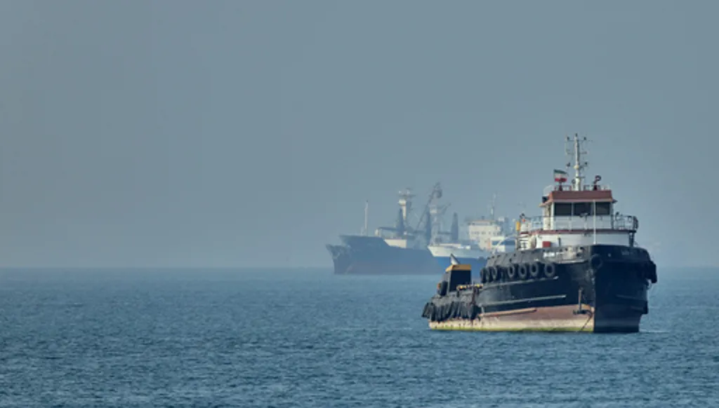 An Iranian tugboat floats in the foreground as cargo ships sit at anchor in the Strait of Hormuz off Bandar Abbas, Iran, Monday, May 4, 2026. (Amirhosein Khorgooi/ISNA via AP)