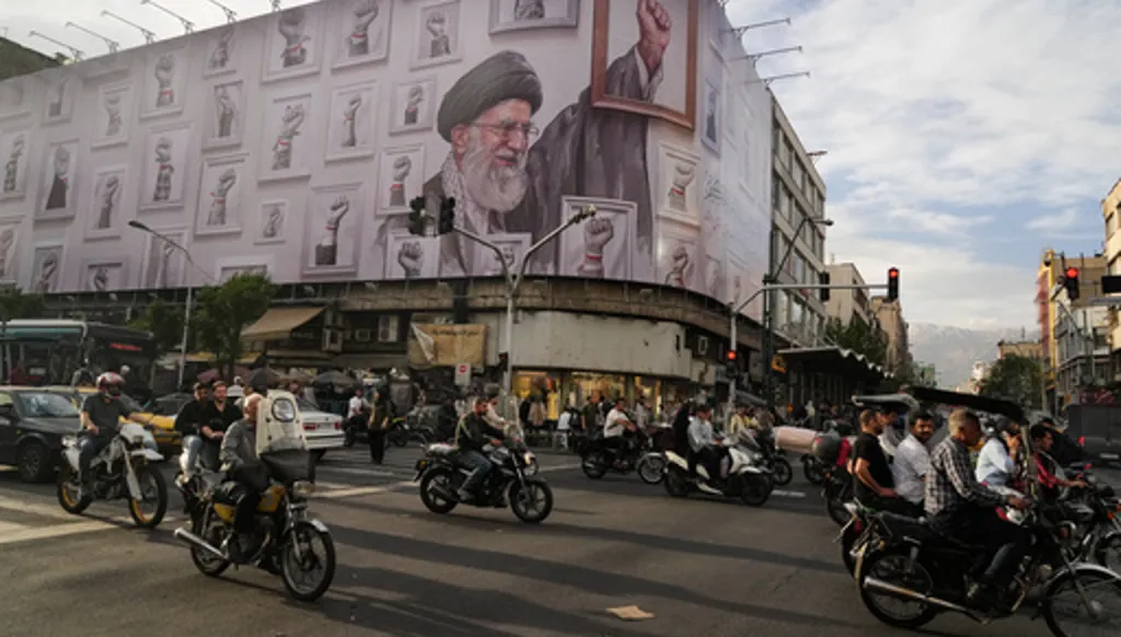 Motorbikes drive past a billboard with graphic showing the late Iranian Supreme Leader Ayatollah Ali Khamenei, who was killed in the U.S. and Israel strikes on Feb. 28, with his framed fist amongst his supporters framed fists in downtown Tehran, Iran, Wednesday, May 6, 2026. (AP Photo/Vahid Salemi)