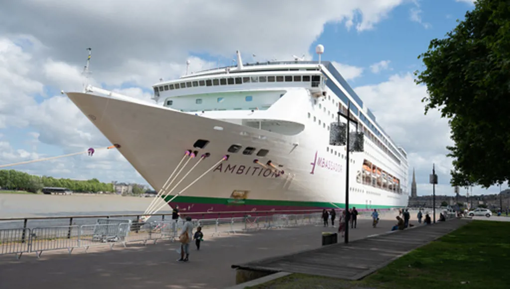 People walk past the British cruise ship Ambition, as French authorities have ordered 1,700 passengers and crew to stay on board due to a gastrointestinal illness outbreak, in Bordeaux, southwestern France, Wednesday, May 13, 2026. (AP Photo/Caroline Blumberg)